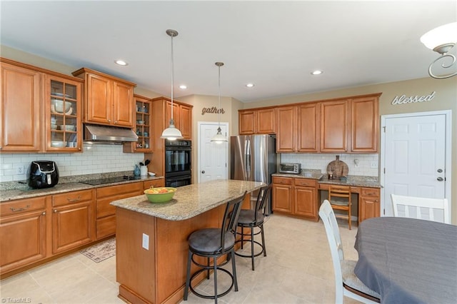 kitchen featuring light stone countertops, decorative backsplash, black appliances, a center island, and hanging light fixtures