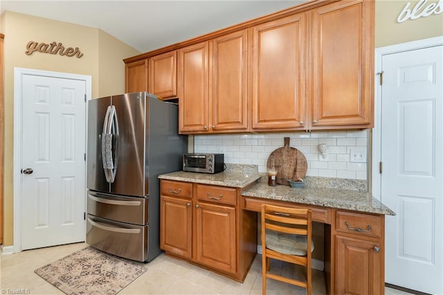 kitchen with light stone countertops, light tile patterned floors, tasteful backsplash, and stainless steel refrigerator