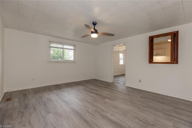 spare room featuring wood finished floors, visible vents, a wealth of natural light, and baseboards