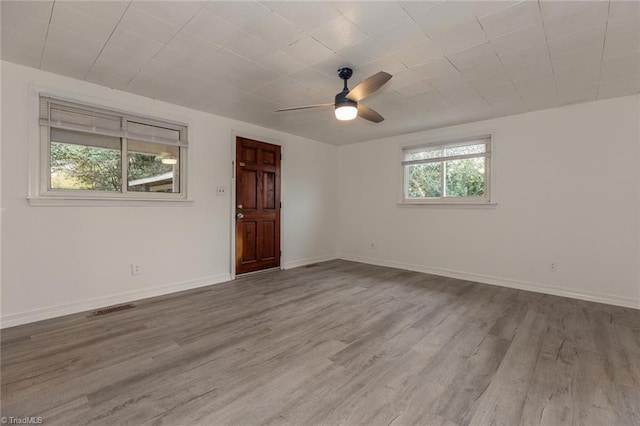 spare room with ceiling fan, visible vents, baseboards, and wood finished floors