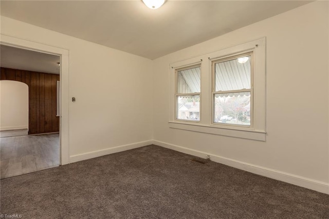 empty room with dark colored carpet, baseboards, and arched walkways