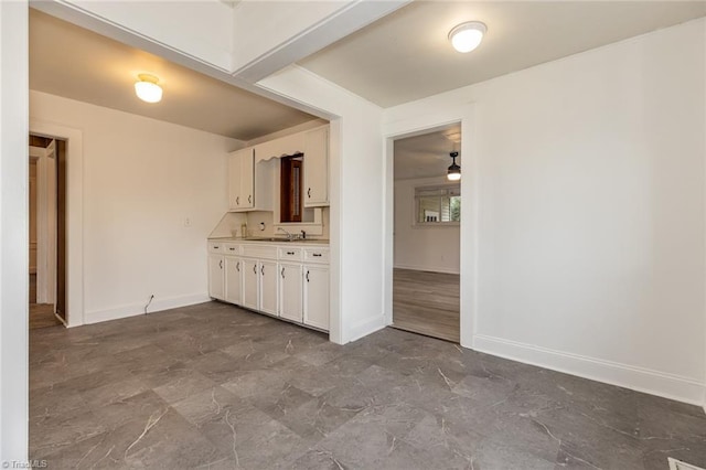 kitchen with white cabinetry, light countertops, baseboards, and a sink