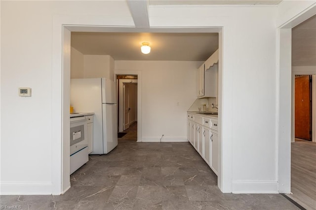 kitchen featuring baseboards, freestanding refrigerator, stove, light countertops, and white cabinetry