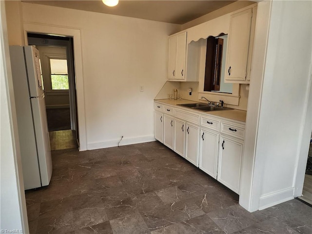 kitchen with baseboards, freestanding refrigerator, a sink, light countertops, and white cabinets