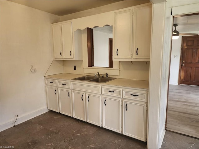 kitchen with a sink, baseboards, light countertops, and white cabinetry