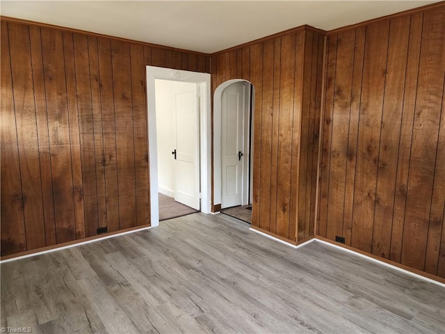 unfurnished bedroom featuring baseboards, arched walkways, wooden walls, and wood finished floors