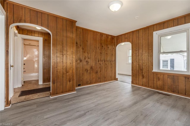 unfurnished room featuring visible vents, wood finished floors, arched walkways, and wood walls