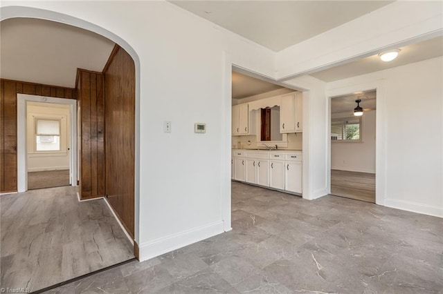 hall with a sink, baseboards, arched walkways, and wood walls