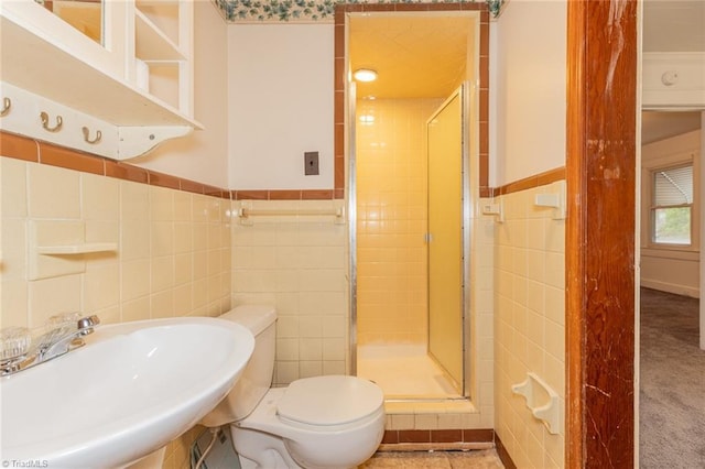 bathroom with a wainscoted wall, toilet, a stall shower, tile walls, and a sink