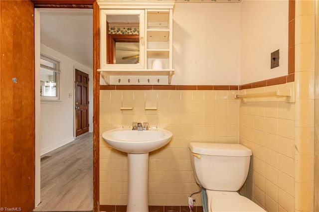 bathroom featuring a wainscoted wall, toilet, a sink, wood finished floors, and tile walls