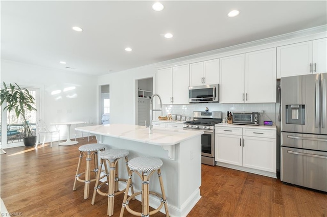 kitchen with dark wood-type flooring, stainless steel appliances, white cabinets, a center island with sink, and decorative backsplash