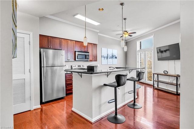 kitchen featuring a kitchen breakfast bar, wood finished floors, a center island, stainless steel appliances, and crown molding