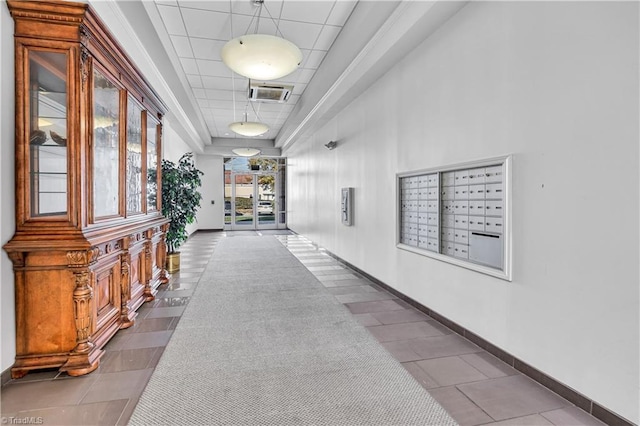 corridor with mail boxes, a tray ceiling, and tile patterned floors