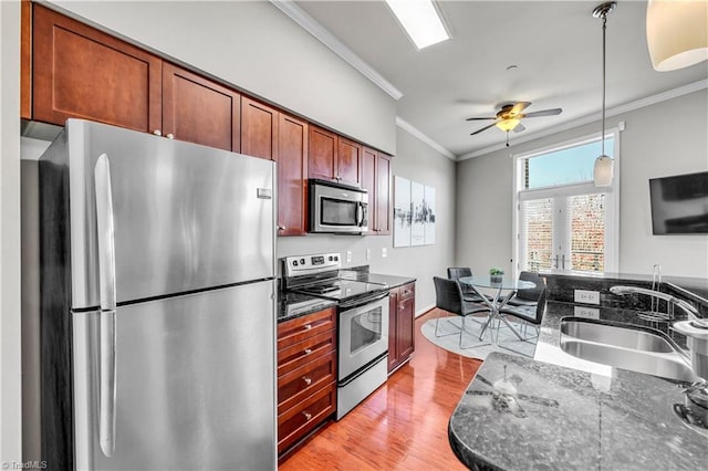 kitchen with light wood-type flooring, stainless steel appliances, dark stone countertops, and sink