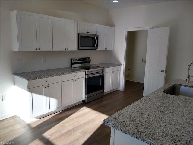 kitchen with appliances with stainless steel finishes, white cabinets, light stone counters, and sink