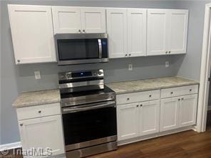 kitchen with appliances with stainless steel finishes, dark hardwood / wood-style flooring, white cabinetry, and light stone countertops