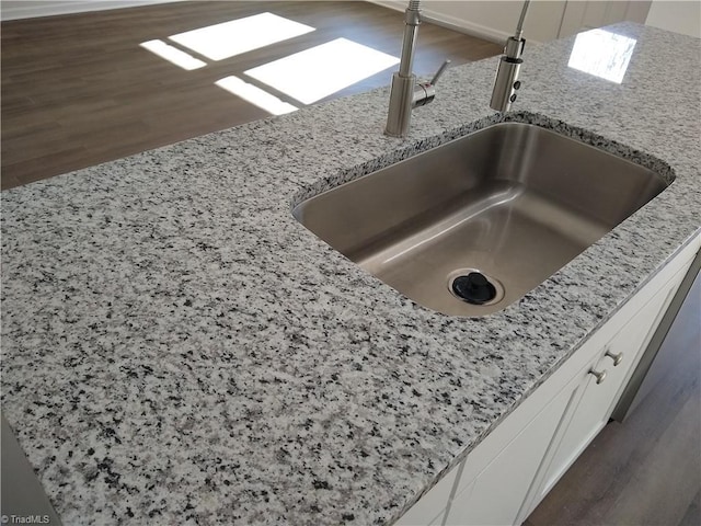 interior details featuring light stone countertops, white cabinetry, and sink