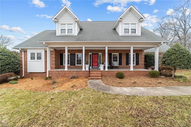 view of front facade featuring a porch, a shingled roof, brick siding, and a front yard