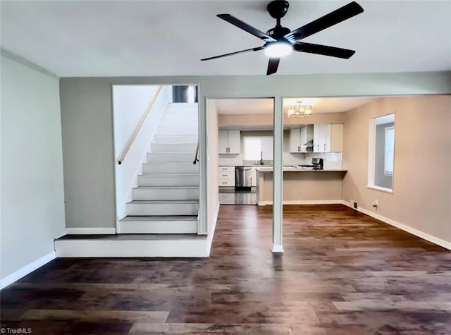 unfurnished living room with ceiling fan with notable chandelier and dark wood-type flooring