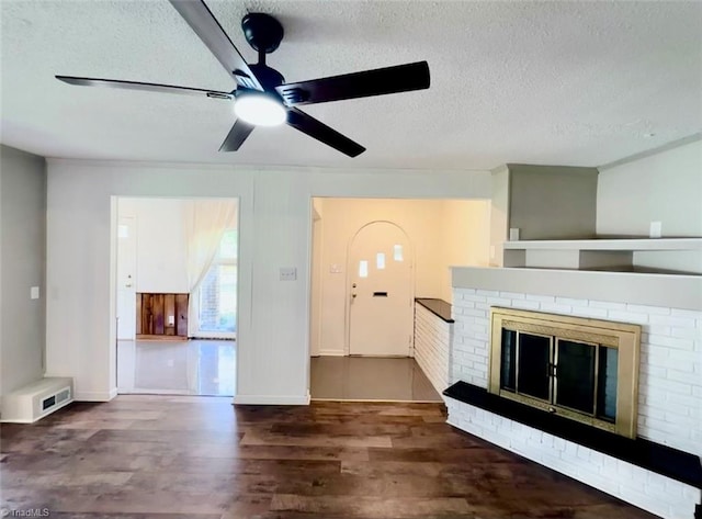 unfurnished living room featuring ceiling fan, a textured ceiling, a fireplace, and dark hardwood / wood-style floors