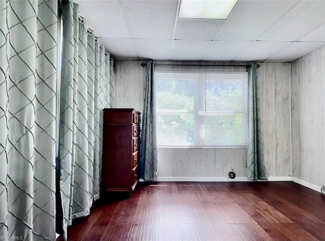 empty room with a drop ceiling and dark hardwood / wood-style flooring