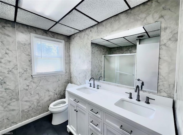 bathroom with a drop ceiling, vanity, toilet, and a shower with door