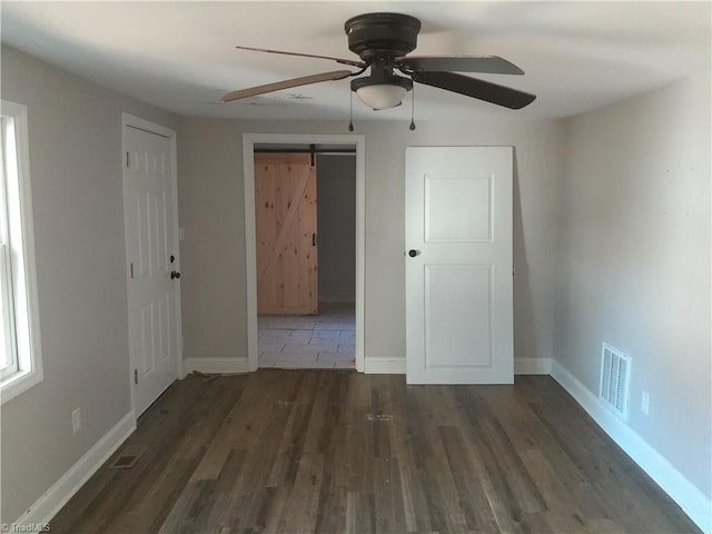 unfurnished bedroom featuring a barn door, ceiling fan, and dark wood-type flooring