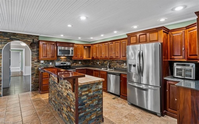 kitchen featuring appliances with stainless steel finishes, arched walkways, a sink, and decorative backsplash