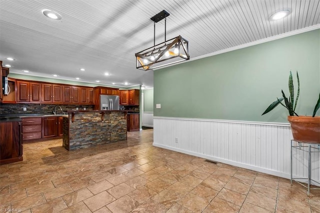 kitchen featuring dark countertops, wainscoting, a kitchen island, a sink, and stainless steel fridge with ice dispenser