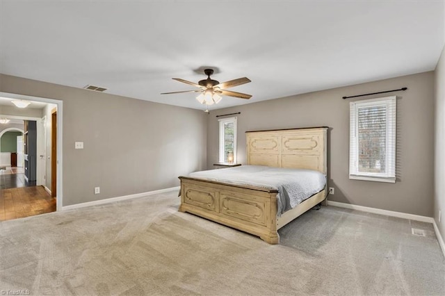 unfurnished bedroom featuring light colored carpet, visible vents, arched walkways, and baseboards