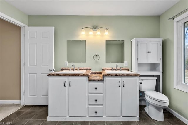 bathroom featuring toilet, double vanity, baseboards, and a sink