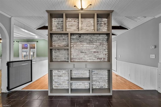 interior space featuring lofted ceiling, a wainscoted wall, arched walkways, and tile patterned floors