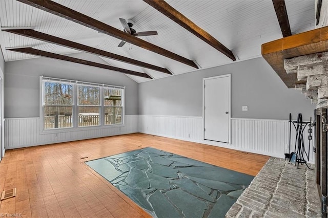 unfurnished living room with lofted ceiling with beams, a wainscoted wall, a ceiling fan, visible vents, and hardwood / wood-style floors