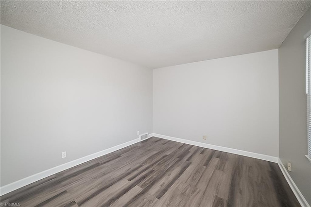 empty room with dark hardwood / wood-style floors and a textured ceiling