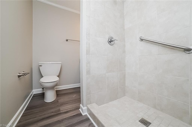 bathroom featuring hardwood / wood-style flooring, toilet, crown molding, and tiled shower