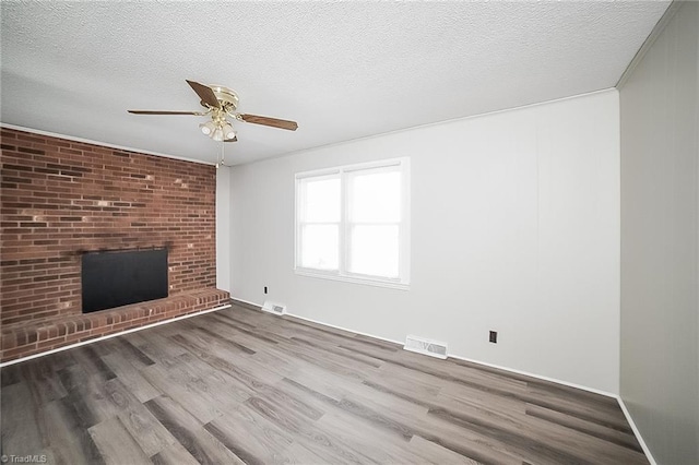 unfurnished living room featuring ceiling fan, hardwood / wood-style floors, a textured ceiling, and a brick fireplace