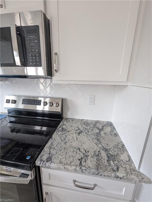 kitchen with appliances with stainless steel finishes, white cabinetry, backsplash, and light stone countertops