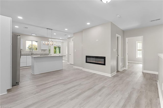 unfurnished living room with a notable chandelier and light wood-type flooring