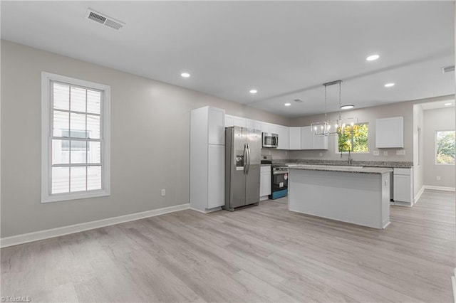 kitchen featuring white cabinets, stainless steel appliances, pendant lighting, light hardwood / wood-style floors, and a center island