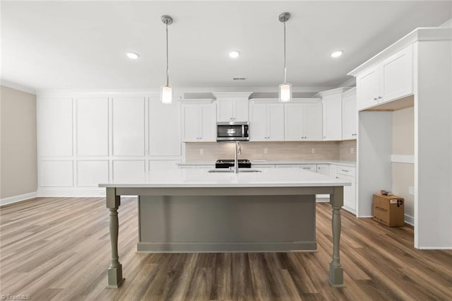 6969 Orchard Path Dr, Clemmons, NC 27012 - kitchen featuring stainless steel microwave, light countertops, backsplash, a center island with sink, and wood finished floors