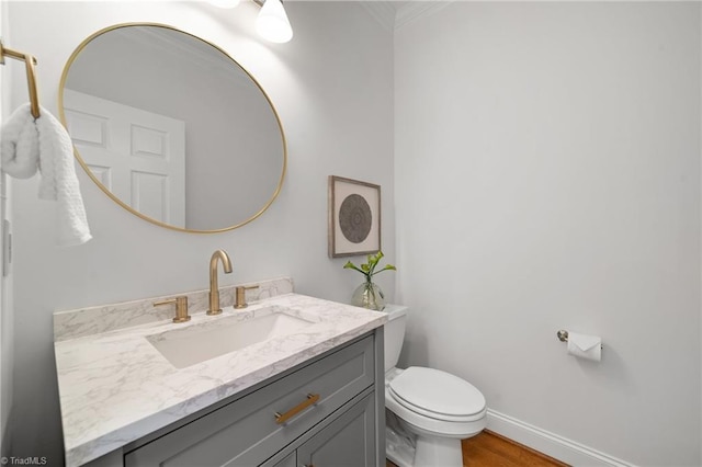 half bath featuring toilet, vanity, crown molding, baseboards, and wood finished floors