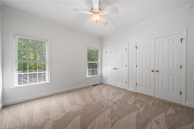 unfurnished bedroom with multiple closets, carpet, crown molding, multiple windows, and baseboards