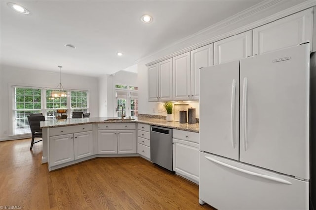kitchen featuring freestanding refrigerator, stainless steel dishwasher, a sink, a peninsula, and plenty of natural light