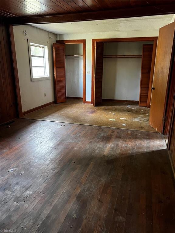 unfurnished bedroom featuring wood ceiling, two closets, and dark hardwood / wood-style flooring