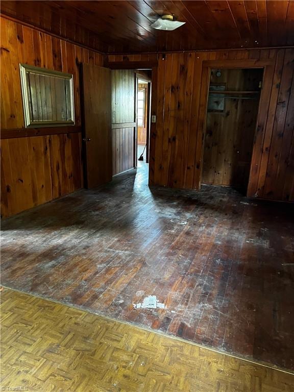 empty room with wood walls, dark parquet floors, and wooden ceiling