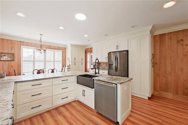 kitchen with light hardwood / wood-style floors, a notable chandelier, kitchen peninsula, appliances with stainless steel finishes, and hanging light fixtures