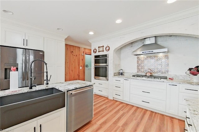 kitchen featuring light hardwood / wood-style floors, stainless steel appliances, light stone countertops, wall chimney exhaust hood, and white cabinetry