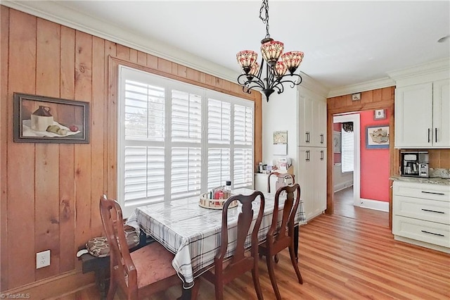 dining space with wooden walls, an inviting chandelier, crown molding, and light hardwood / wood-style floors