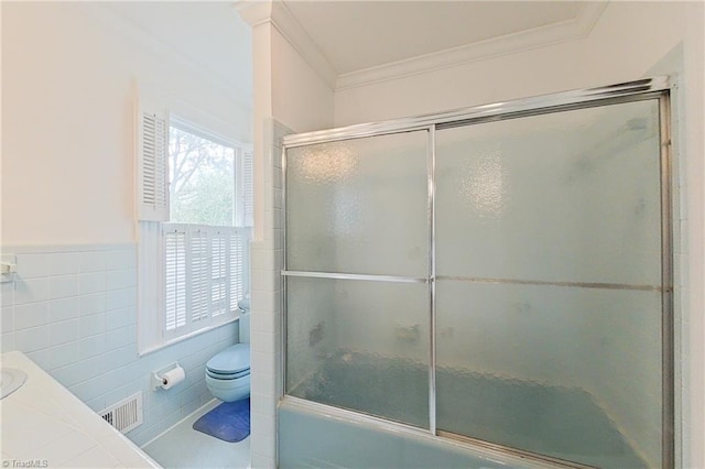 bathroom featuring tile walls, shower / bath combination with glass door, toilet, and crown molding