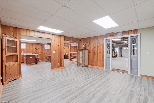 basement featuring a paneled ceiling, wood walls, and light wood-type flooring